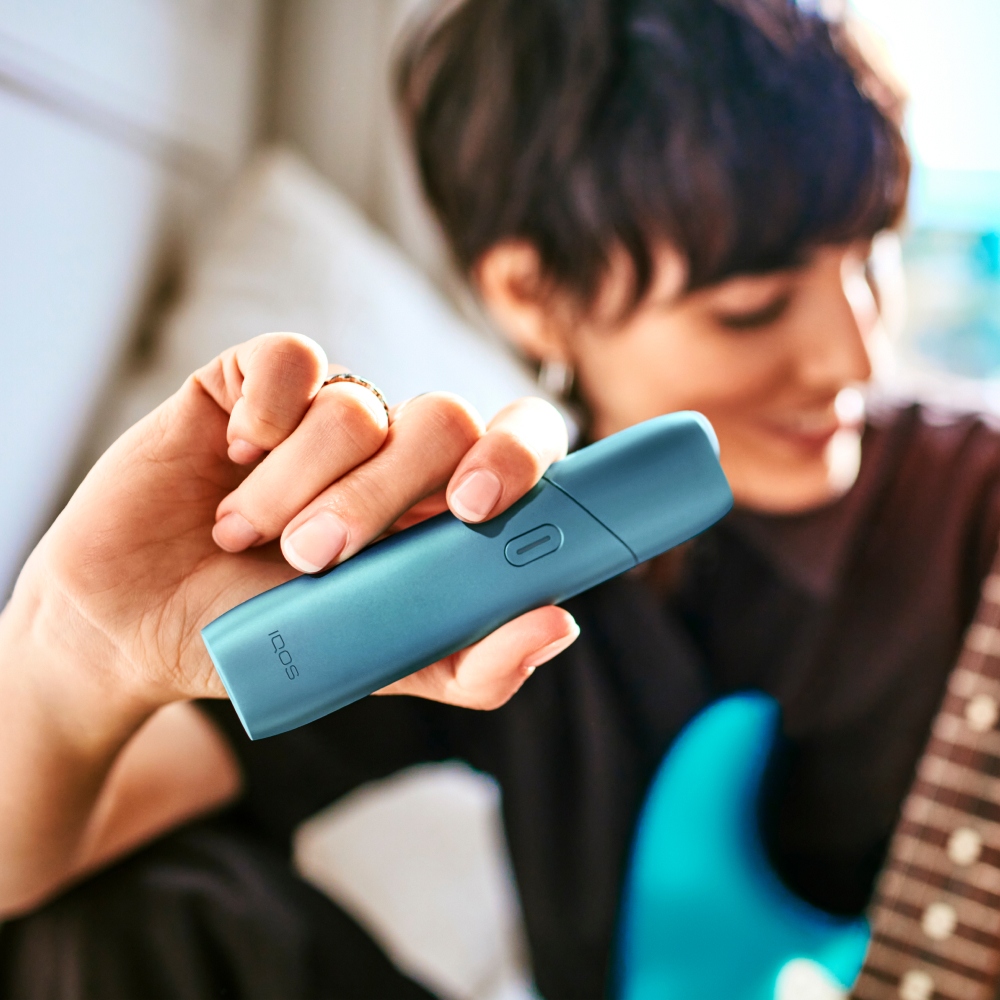 Mujer tocando guitarra mientras sostiene un IQOS Originals One