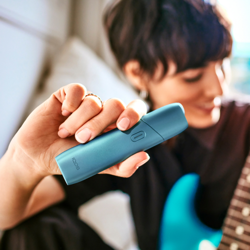 Mujer tocando guitarra mientras sostiene un IQOS Originals One