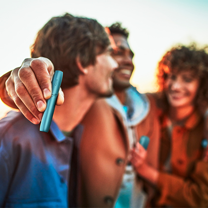 Personas abrazandose sosteniendo un IQOS ORIGINALS DUO turquesa