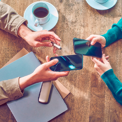 Manos sosteniendo telefonos intercambiando un código de referido IQOS para ocmprar un dispositivo nuevo con descuento.